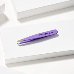 Tweezerman pinza mini junto a moneda para mostrar tamaño compacto